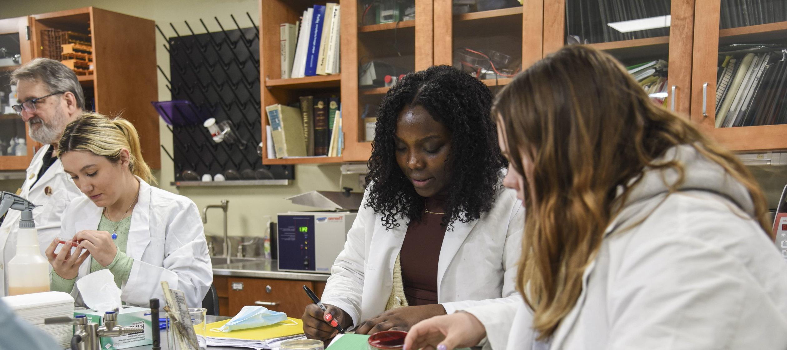 Students in white lab coats work in the microbiology lab.